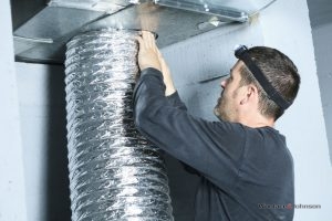A technician provides HVAC parts replacement on an air duct.