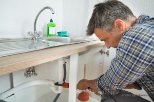 A plumber conducts kitchen and bathroom repairs on a sink.